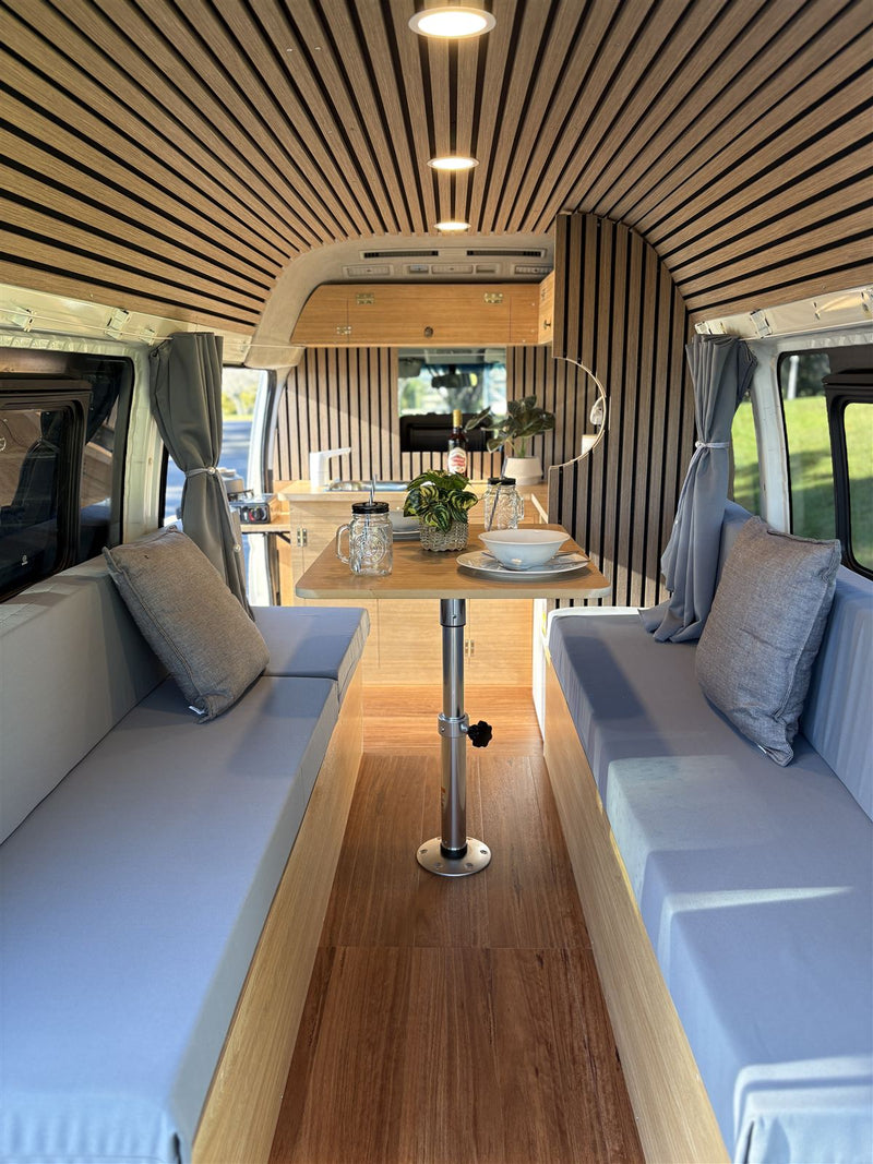 Campervan lounge with two facing bench seats, table set for dinner, timber slat ceiling and walls