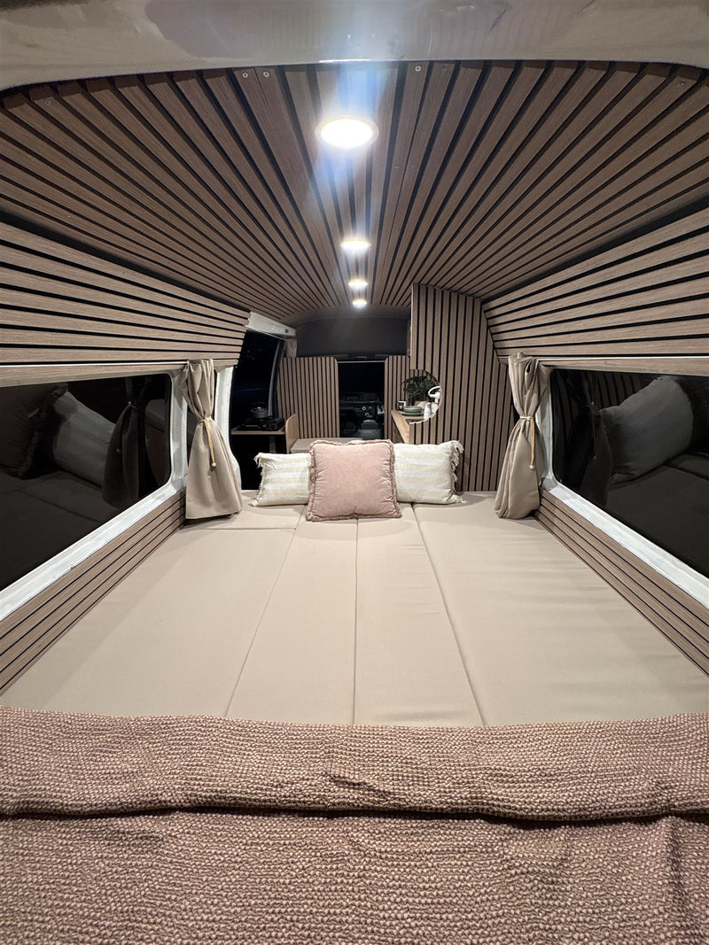 Campervan interior at night with the full-width bed made up, cushions and warm LED downlights