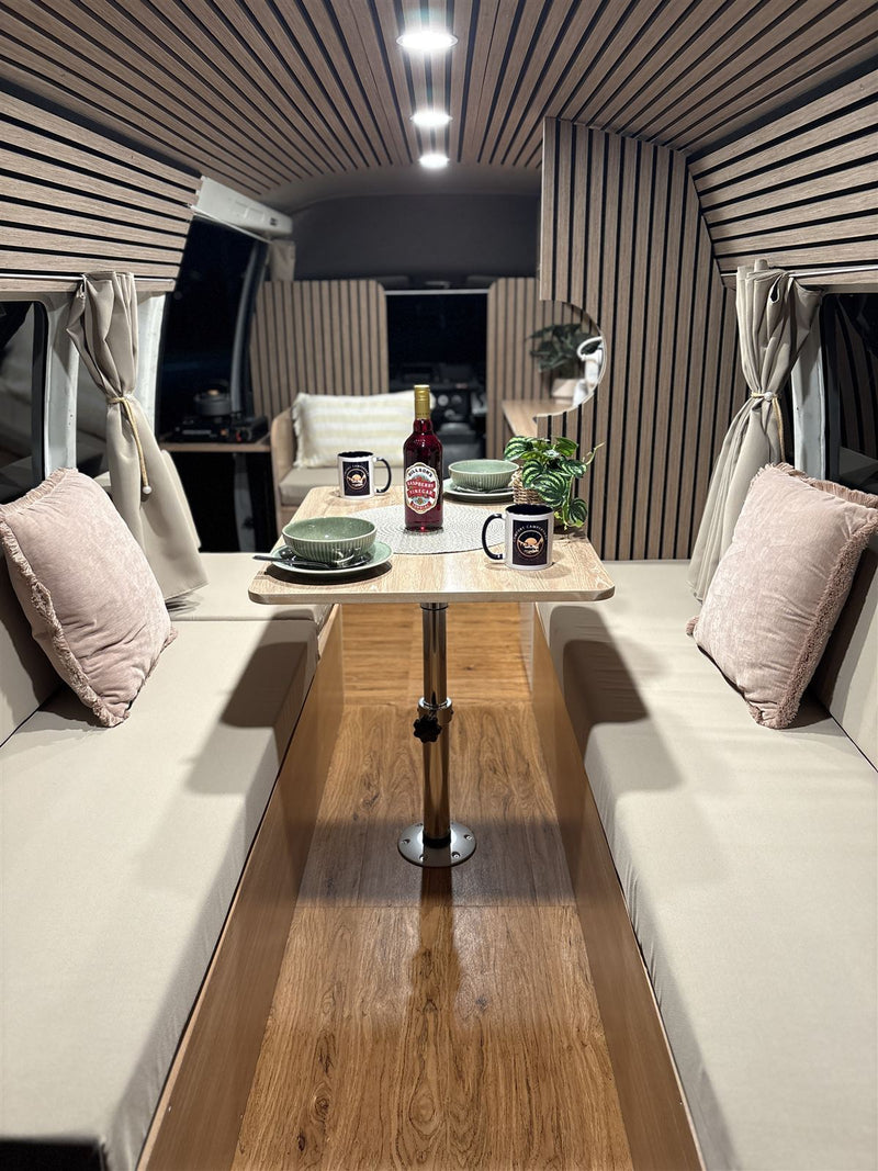 Campervan dining table set with bowls and Comfort Campervans mugs between two upholstered bench seats
